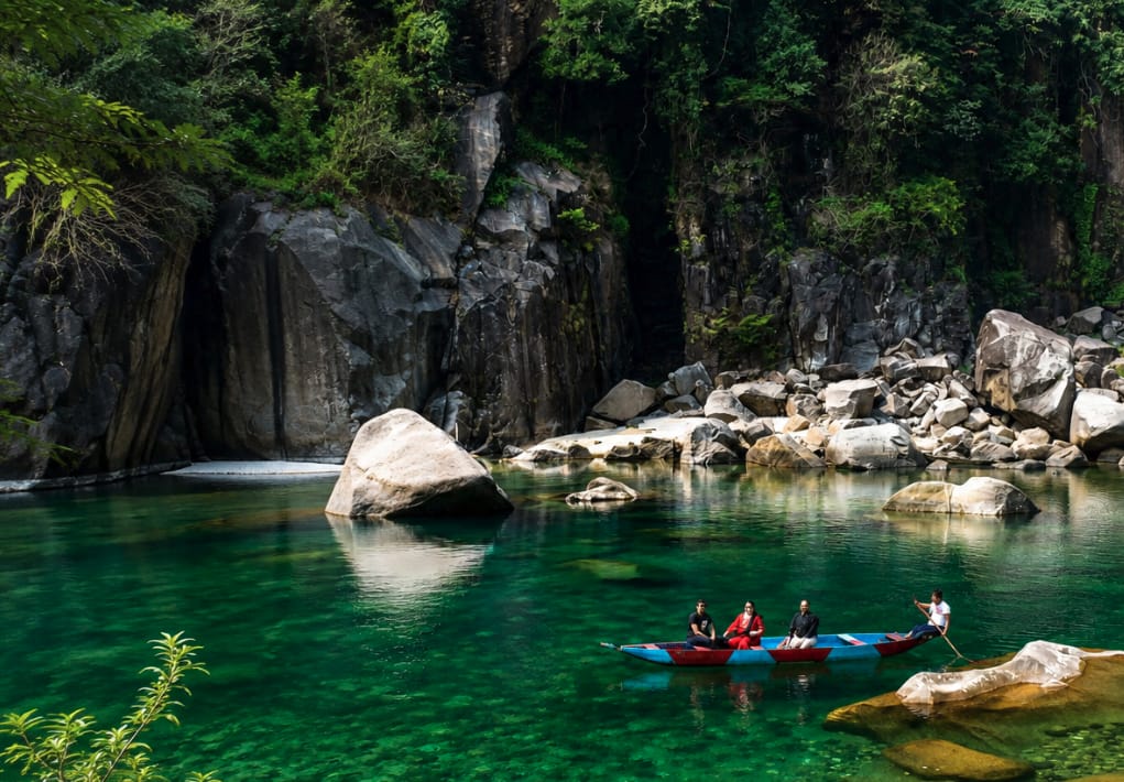 People boating on clear water beneath rocky cliffs