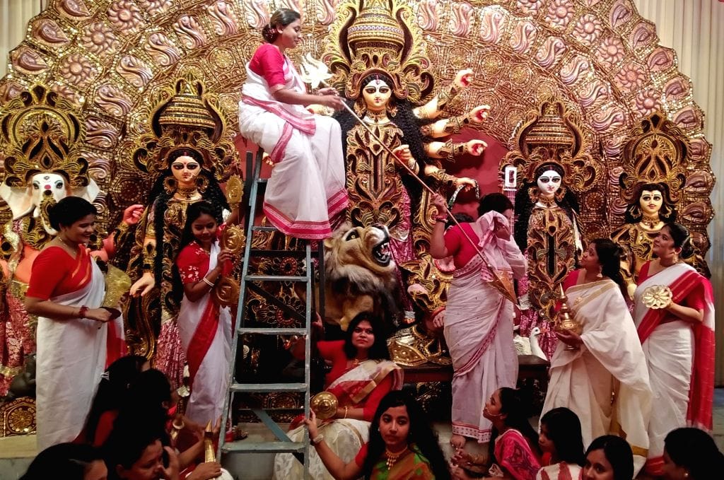 Women in red and white saris celebrating beside Durga idols