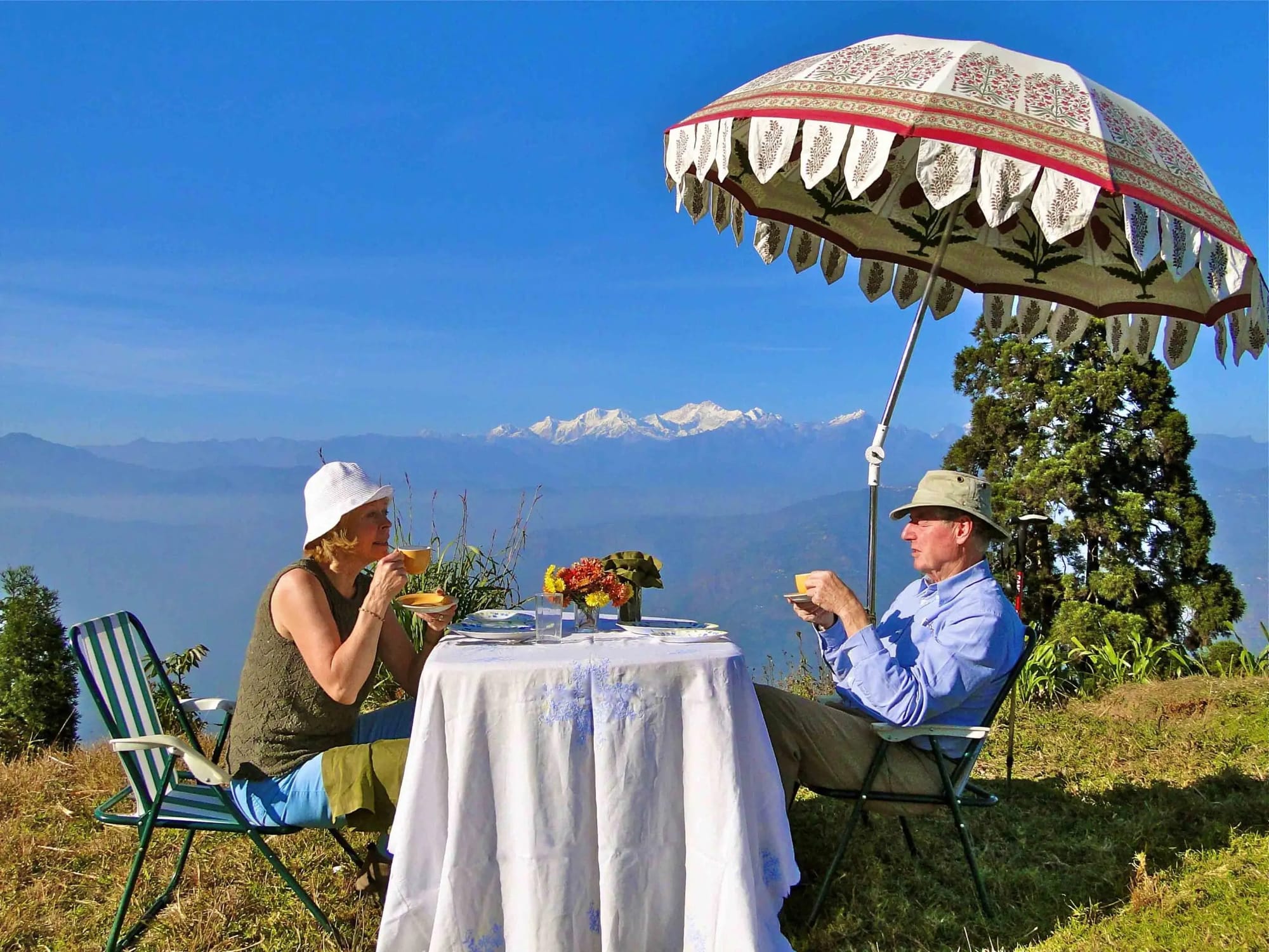 Two guests taking tea beneath a parasol overlooking mountains