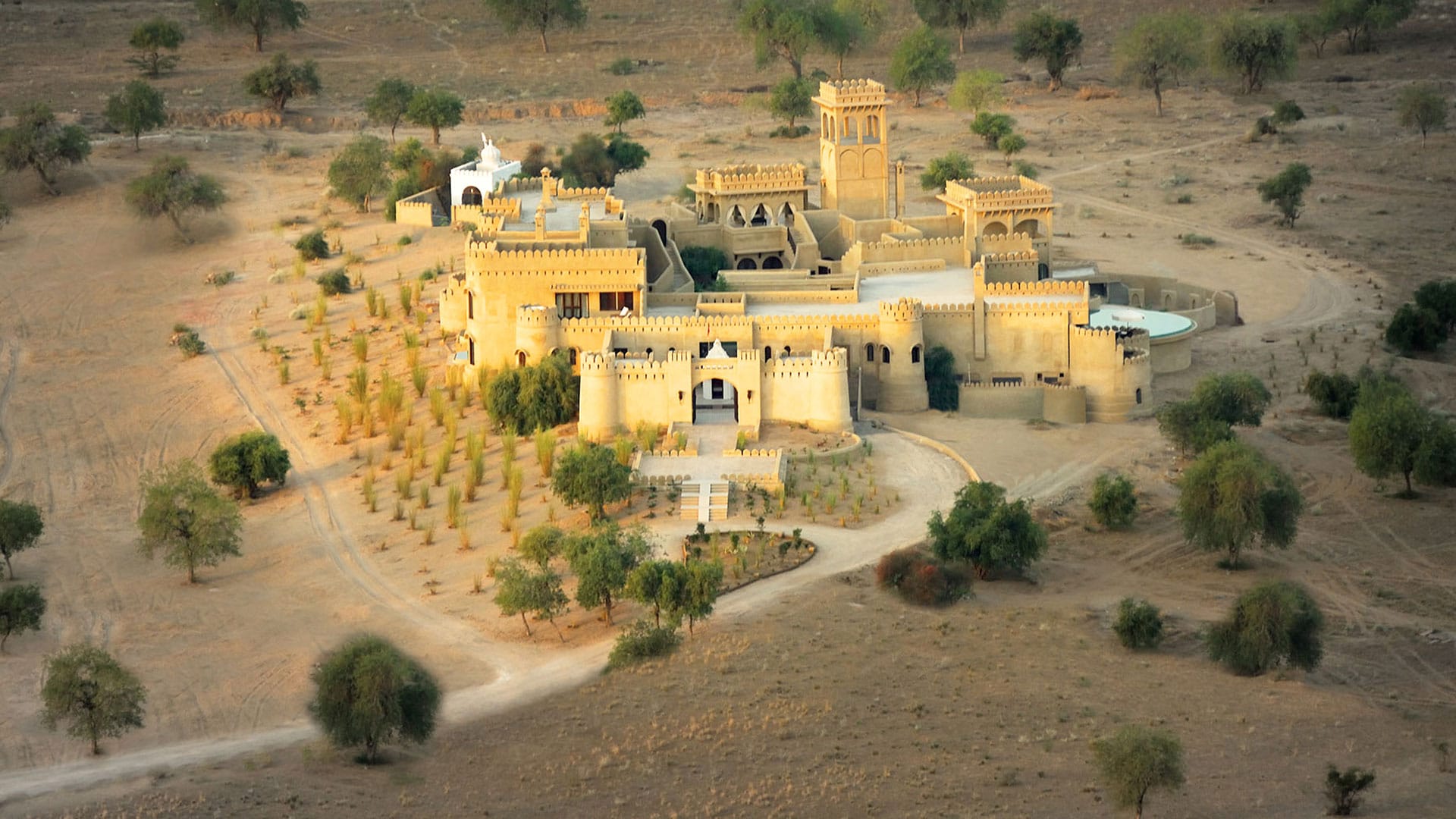 A sand-colored fort surrounded by dry countryside and scattered trees