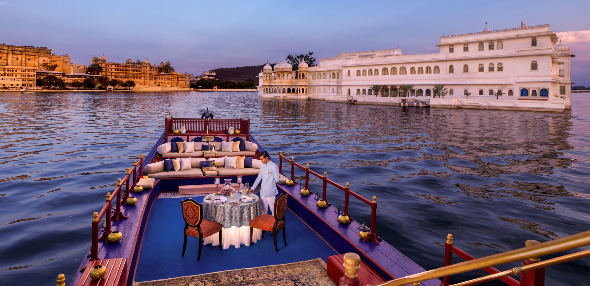 A dining table aboard a boat facing a white lakeside palace
