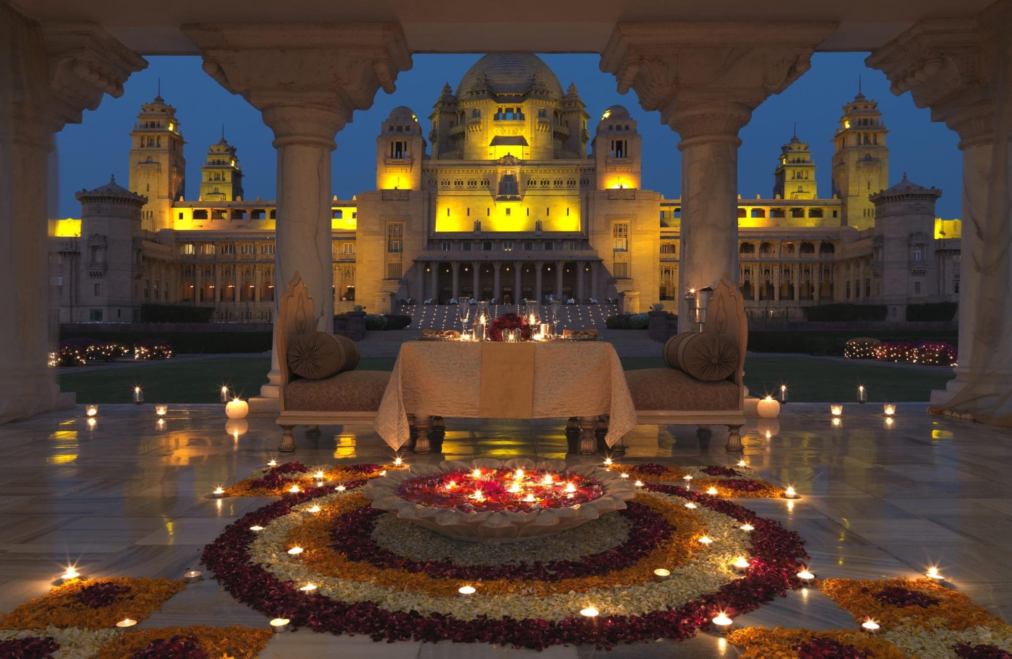 A candlelit dining table beneath carved arches facing an illuminated palace