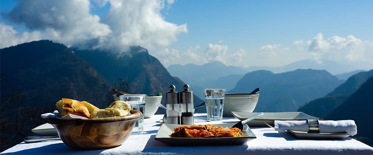 A meal set on an outdoor table overlooking layered mountain peaks