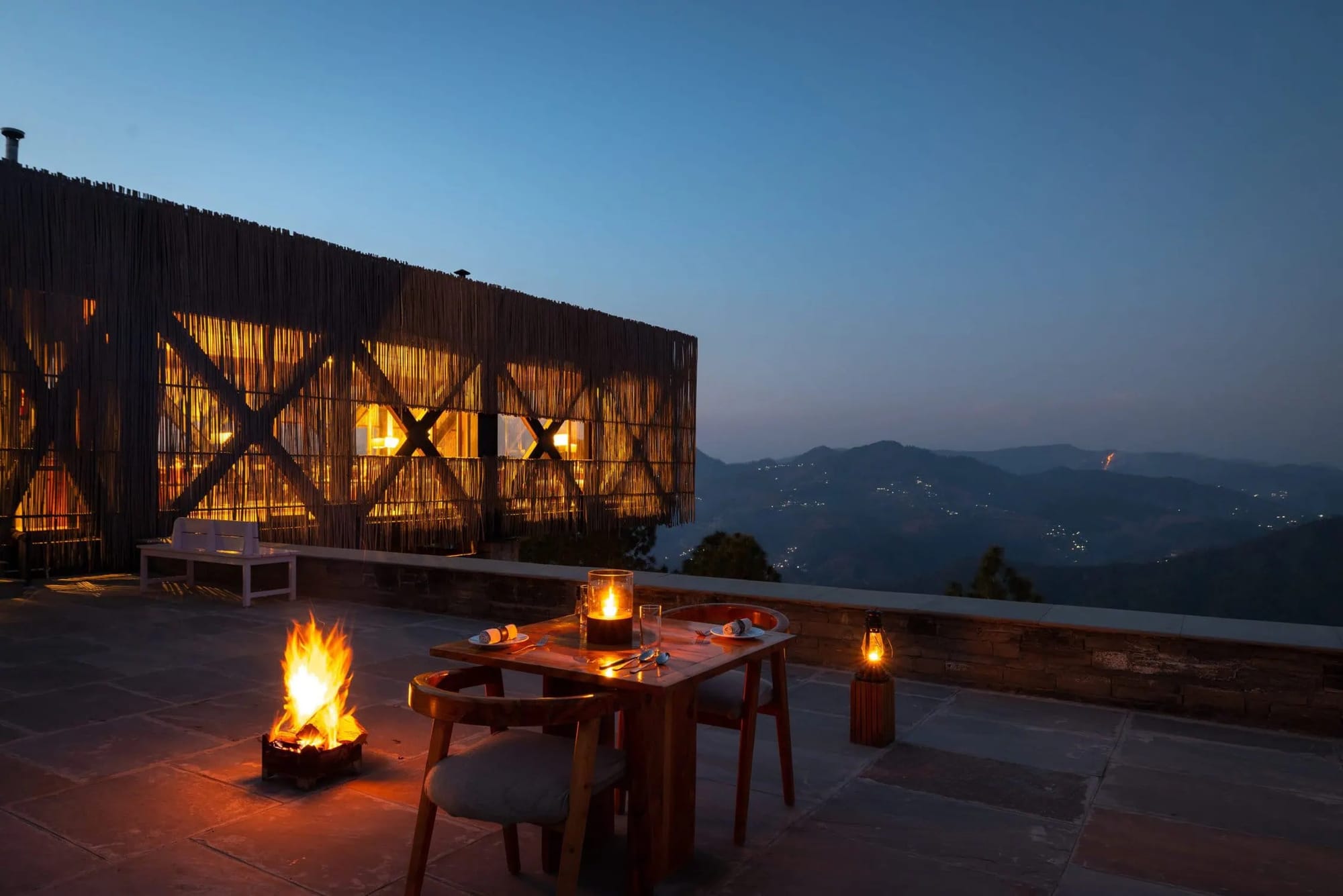 A fire and candlelit table beside a modern lodge overlooking mountains